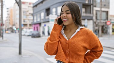 Gülümseyen genç bir İspanyol kadın şehrin bir caddesinde telefonla konuşuyor, güzel ve kendine güvenen bir kadın..