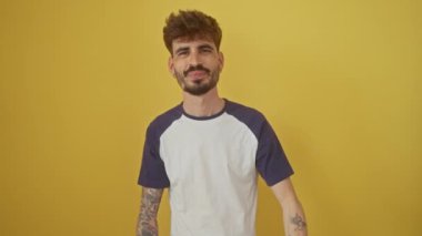 Neşeli, genç İspanyol bir adam izole edilmiş sarı arka planda duruyor. Sağlıklı diş bakımını işaret ediyor ve gülümsüyor.