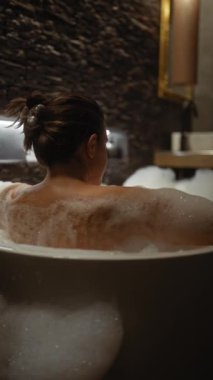 Bir kadın lüks bir banyoda sakin bir köpük banyosundan zevk alır. Rahatlama ve kendine bakımı çağrıştırır..
