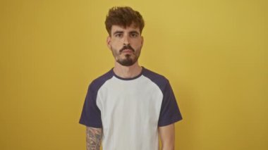 Genç ispanyol adam ayakta duruyor, yanaklarını şişiriyor çılgın, komik bir yüz ifadesi için, izole edilmiş sarı arka planda ağzı şişmiş.