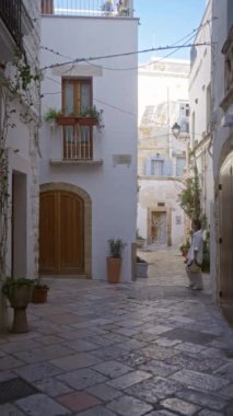 Genç İspanyol bir kadın polignano 'nun büyüleyici sokaklarında yürüyor. Bir kısrak, puglia, İtalya, geleneksel mimari unsurlar, canlı saksı bitkileri ve rahat bir ortam..