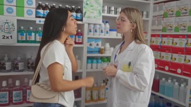 Eczanede sohbet eden iki kadın, biri eczacı, diğeri de ilaç raflarıyla çevrili bir müşteri..