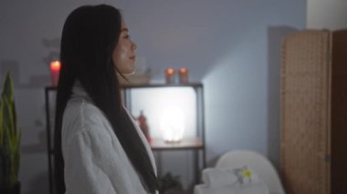 Huzurlu bir spa odasında dinlenen bir kadın Çin 'de bir sağlık merkezinde beyaz bir bornoz giyiyor. Arka planda hafif ışıklandırma, bitkiler ve rahat mumlar var..