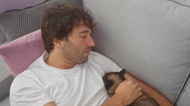 Evde kanepede siyam kedisiyle sarılan rahat bir adam..