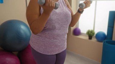 Spor salonunda spor salonunda halterlerle egzersiz yapan bir kadın, iyi ışıklandırılmış bir odada egzersiz ekipmanıyla spor salonunda güç ve zindelik gösterisi yapıyor.