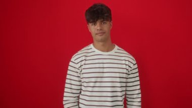 Çizgili tişört giyen İspanyol genç adam izole edilmiş kırmızı arka planda güvenle duruyor, küçük beden kavramını göstermek için el ve parmaklarıyla işaret ediyor.