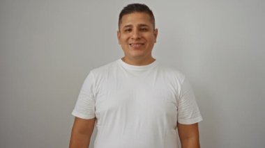 Genç İspanyol adam izole edilmiş beyaz bir arka planda arkadaşça ve mutlu bir ifadeyle el sallıyor.