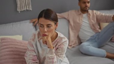 Kadın düşüncesi ve erkek oturma odasında bir kanepede oturuyor, modern bir ev ortamında ilişki sorunları ve duygularını ifade ediyor.