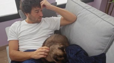 Düşünceli genç bir adam evdeki kanepede siyam kedisiyle oturur, sıradan, evcil bir sahneyi somutlaştırır..