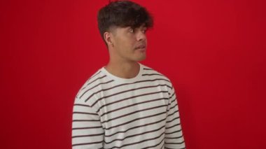 Gizli bilgi veren, çizgili tişört giyen genç İspanyol adam. El pençe divan duran, kırmızı arka planda kötü niyetli konuşmalar ve konuşmalar fısıldayan.