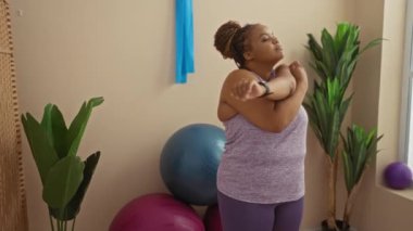 Spor salonunda spor topları ve bitkilerle esneyen, mor bir atlet giyen ve taytlı bir kadın, evde sağlıklı bir yaşam tarzını kucaklıyor..