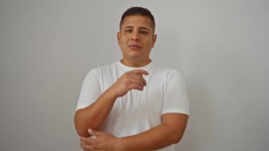 Beyaz bir arka planda, beyaz bir gömlekle gülümseyen ve güvenle poz veren genç İspanyol bir adam, rahat ve rahat bir tavır sergiliyor.