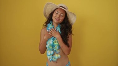 Yaz şapkalı genç Çinli kadın ve Hawaii leyleği, elleri göğsünde, sarı arka planda sağlığına gülümseyen minnettar bir jest sergiliyor.