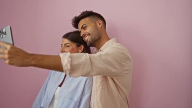 Kadın ve erkek pembe bir arka plana karşı selfie çekiyorlar, mutlu ve sevgi dolu bir ilişki sergiliyorlar..
