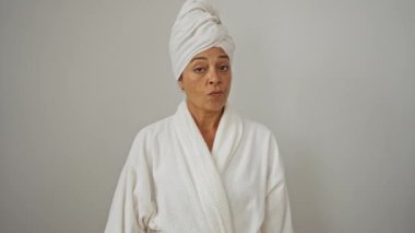 Havlu ve bornoz giymiş orta yaşlı bir kadın öfkeli bir ifadeyle baş parmak hareketi yapıyor, mutsuz görünüyor ve izole beyaz arka planda negatif duygular gösteriyor.