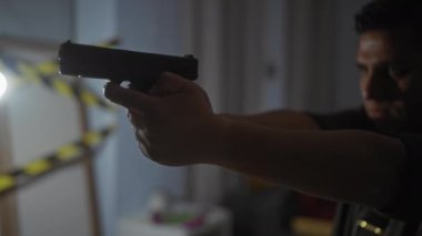 İspanyol bir adam tabancayı evin içine doğrultuyor. Dikkatli bantla tabancaya yakın çekim yapıyor. Loş ışık, gergin bir suç mahalli ortamı yaratıyor..