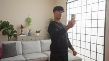 Yakışıklı İspanyol adam, bitkilerle ve çağdaş dekorlarla dolu, parlak, modern bir oturma odasında selfie çekiyor..