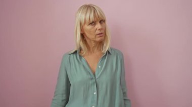 Orta yaşlı sarışın kadın tişört giyiyor baş ağrısı ve baş ağrısı yüzünden stres altında. Stres altında ve hastalıktan muzdarip izole edilmiş pembe arka planda acı çekiyor.