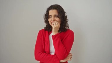 Genç İspanyol kadın gergin bir şekilde ayakta duruyor, elleri ağızda tırnak yiyor, izole edilmiş beyaz arka planda endişe ve stres gösteriyor, panik ve duygusal problemlerle karşı karşıya.