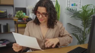 Ofisteki İspanyol kadın gazete okuyor, mutlu ve çekici görünüyor, bitkilerle çevrili ve kapalı bir masada çalışıyor..