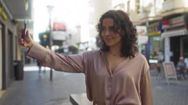 Şehir sokağında duran çekici bir kadın akıllı telefonuyla selfie çekiyor ve şehir hayatının özünü yakalıyor..