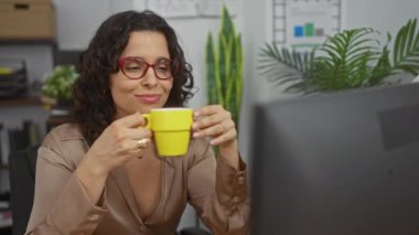 Çiçekler ve çizelgelerle dolu bir ofiste çalışırken şık giyimli bir kadın kahve içer, kırmızı gözlük takar..