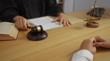 Elinde tokmak ve kitapla mahkeme salonunda müvekkilinin ellerinin olduğu bir masada yasal teraziler ve kapalı masa kağıtları olan bir yargıç.