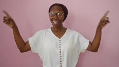 Gözlüklü, genç, Afro-Amerikalı bir kadın pembe bir arka planda, yüzünde hayret verici bir gülümsemeyle dikiliyor.