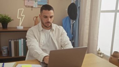 Modern bir oturma odasında dizüstü bilgisayarıyla çalışan ve rahatlayan genç bir İspanyol..