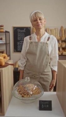 Fırında önlük giymiş, ekmek ve hamur işleriyle çevrili bir kadın.