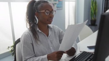 Modern bir ofiste belge okuyan bir kadın, kendinden emin bir gülümsemeyle verileri analiz ediyor, kapalı alanda profesyonel ortamı ve üretken çevreyi vurguluyor..