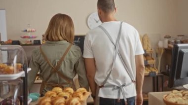 Kadın ve erkek fırında önlük takıyor, taze ekmek ve hamur işlerinin arasında mutlu mesut duruyorlar.