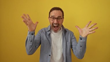 İspanyol orta yaşlı, gözlüklü, mutlu kazananı kutlayan gözlüklü, zafer kazanan, gülümseyen, izole edilmiş sarı arka planlı, neşeli zafer ve pozitif enerjili bir adam.