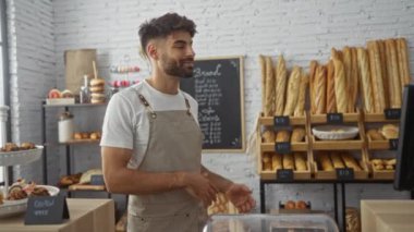 Sakallı genç adam pastanenin içindeki ekmeği çeşitli ekmek somunları ve hamur işleriyle gösteriyor.
