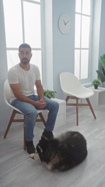 Günlük kıyafetli genç bir İspanyol bir adam veteriner kliniğinin parlak bekleme odasında köpeğini rahatlatıyor..