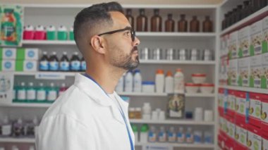 Eczacı üniformalı, kendine güvenen, yan profilde gülümseyen eczanede poz veren, kendine güvenen genç bir İspanyol.