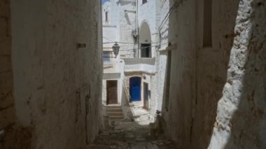 Güneşli bir günde, Ostuni, İtalya 'da manzaralı, kemerli kapıları ve dar kaldırımlı kaldırım taşları olan antika beyaz binalar..