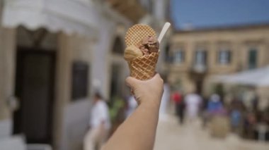 Güneşli bir günde el ele tutuşan dondurma külahı eski bir kasaba olan Ostuni, Puglia, İtalya 'da. Arka planda bulanık insanlar ve binalar var..
