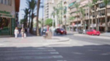 Güneşli bir günde yürüyen kadınlar, binalar, arabalar, palmiye ağaçları ve kentsel çevre ile odaksız sokak sahnesi