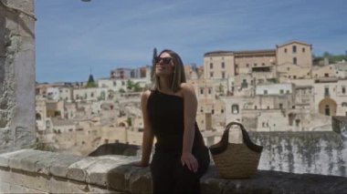 Genç İspanyol kadın güneşli bir günün tadını çıkarıyor. Materya, İtalya 'da eski güzel bir kasaba bakış açısıyla. Saman çantasıyla ve arka planda tarihi şehir manzarasıyla..