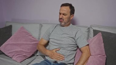 Evdeki oturma odasındaki koltukta oturan adamın karnı ağrıyor.