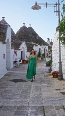 Latin kökenli genç bir kadın alberobello, İtalya 'da sokakta yürüyor, beyaz duvarları ve konik çatıları olan geleneksel trulli evleri sergiliyor..