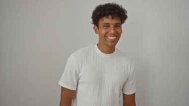 Beyaz tişörtlü genç adam olumlu onay işareti gösteriyor, izole edilmiş arka planda mutlu bir şekilde gülüyor.