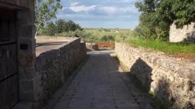 Güneşli bir günde İtalya, Puglia 'da manzaralı bir kırsal manzaraya götüren antik taş duvarlarla çevrili taşra yolu, kırsal Avrupa' nın doğal güzelliğini vurguluyor..