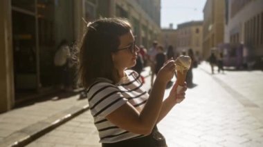 Genç İspanyol kadın, güneşli caddelerde dondurma külahının keyfini çıkarıyor. Lecce, puglia, İtalya, çizgili gömlek ve güneş gözlüğü takıyor..