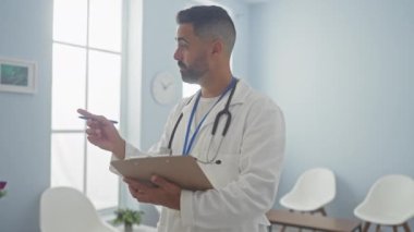 Beyaz laboratuvar önlüklü yakışıklı İspanyol, parlak bir klinik odasında bir panoya yazı yazıyor..