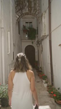 Genç bir İspanyol kadın locorotondo, puglia, İtalya 'nın büyüleyici beyaz sokaklarında yürüyor, etrafı saksı bitkileri ve tarihi mimariyle çevrili..