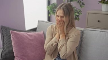 Kanepede oturan genç sarışın kadın gülüyor ve utanıyor kıkırdıyor elleriyle ağzını kapatıyor, dedikodu ve skandal konsepti evde.