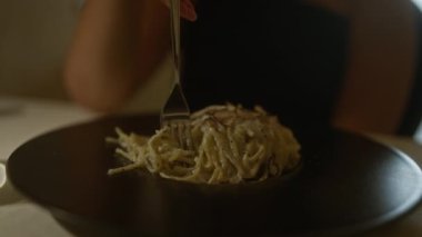 Genç bir kadın, kapalı bir İtalyan restoranında ağız sulandıran makarna tabağına ve rahat sofraya odaklanmış lezzetli bir spagetti tabağının tadını çıkarıyor..