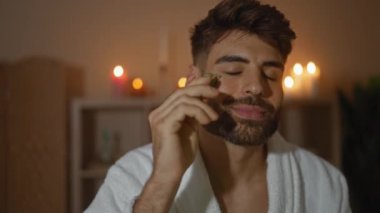 Sakallı yakışıklı genç adam spa 'da rahatlıyor, yeşim taşı kullanıyor, mum ışığında güzellik salonunda.